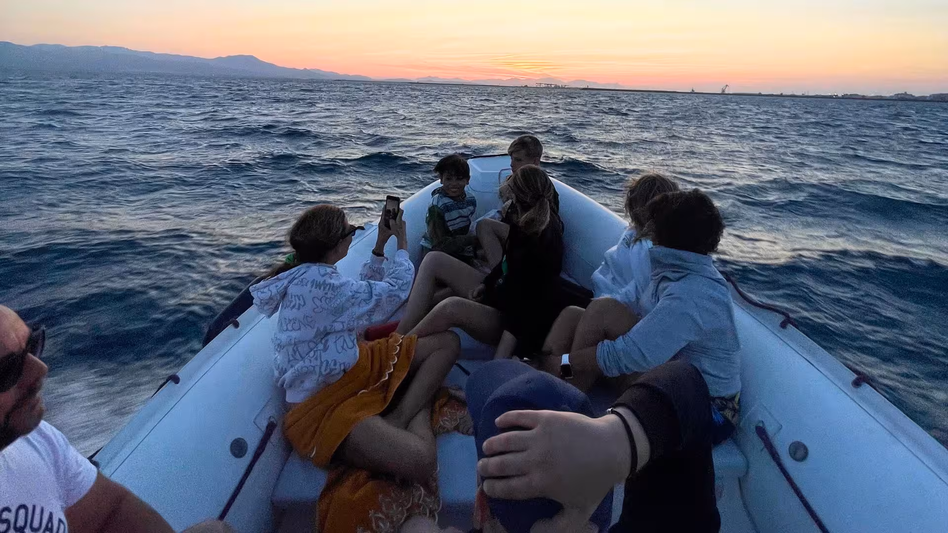 Group enjoying a sunset dinghy tour off Cagliari's coast, capturing vibrant skies and ocean waves.