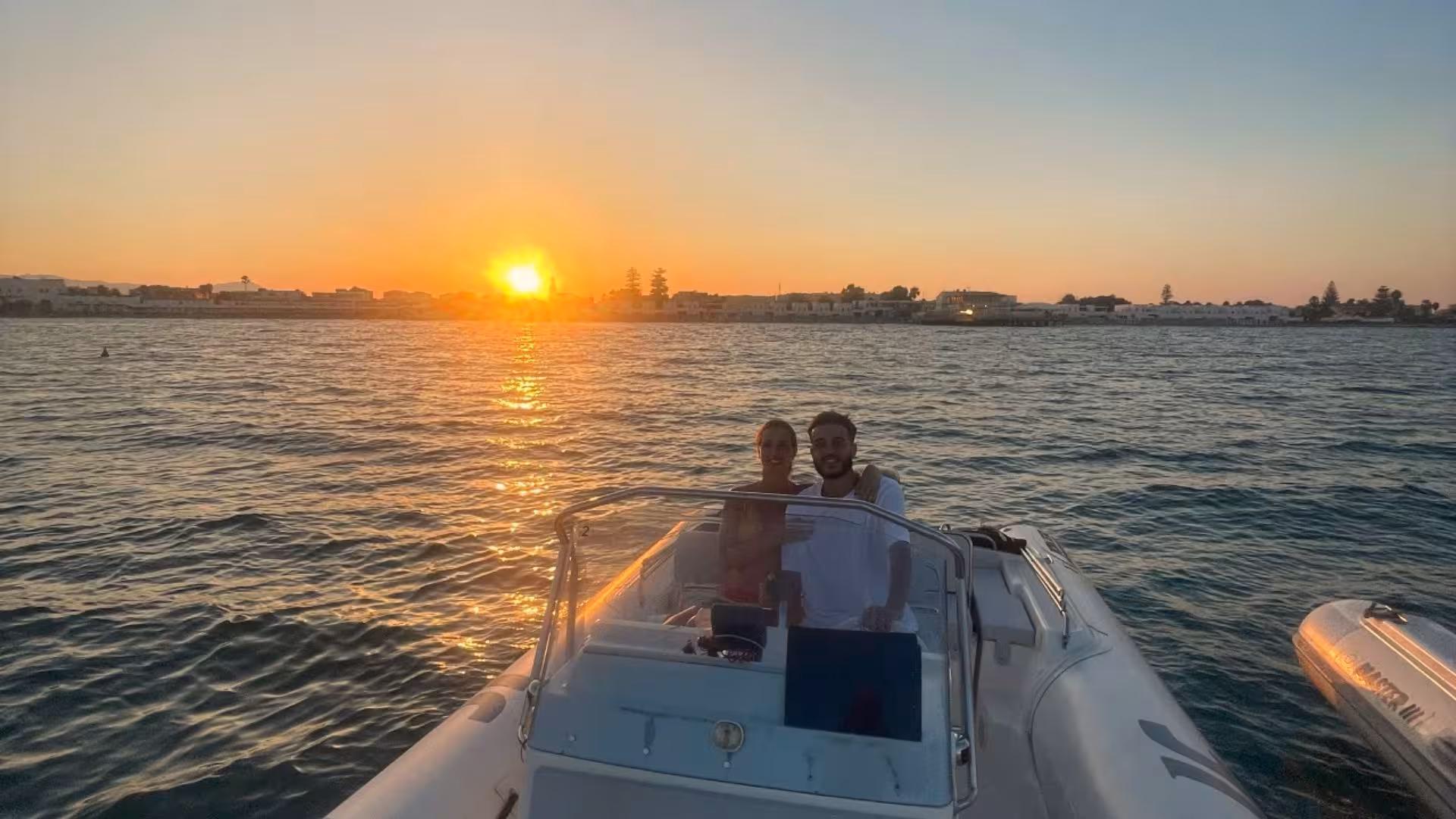 Couple aboard a dinghy enjoy a romantic sunset near Cagliari, perfect for a Sardinian evening escape.