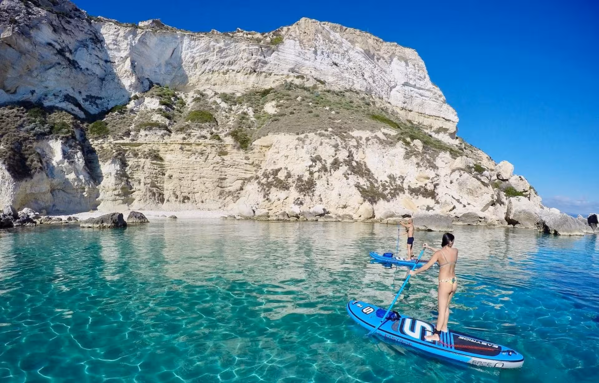 Paddleboarders glide on clear turquoise waters near the stunning cliffs of Sella del Diavolo, Cagliari SUP tour.