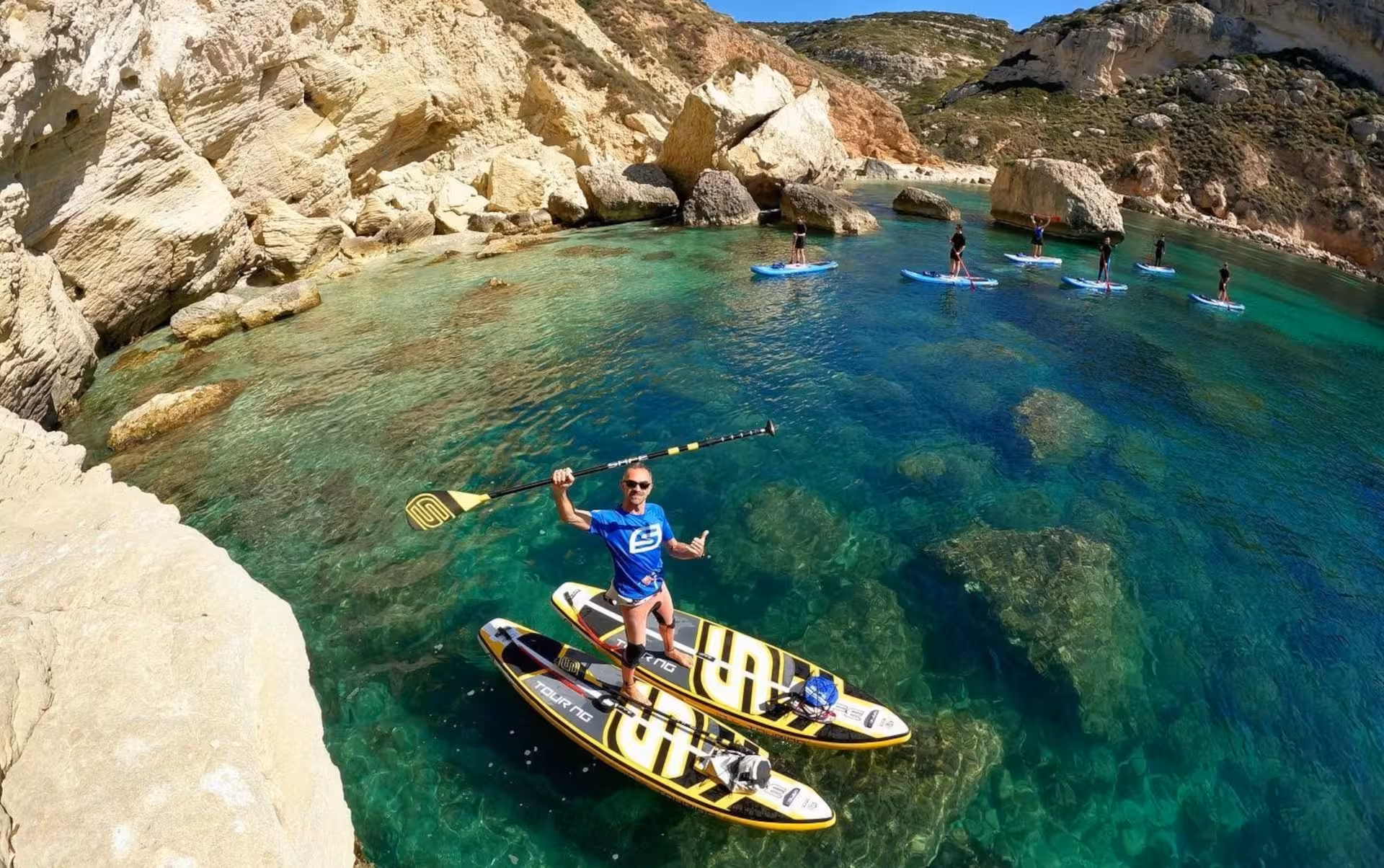 Group enjoying SUP tour in Cagliari's crystal-clear waters near Sella del Diavolo, showcasing vibrant coastal scenery.