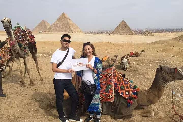 Couple on private layover tour from Cairo Airport to Giza Pyramids, posing by camels in the desert