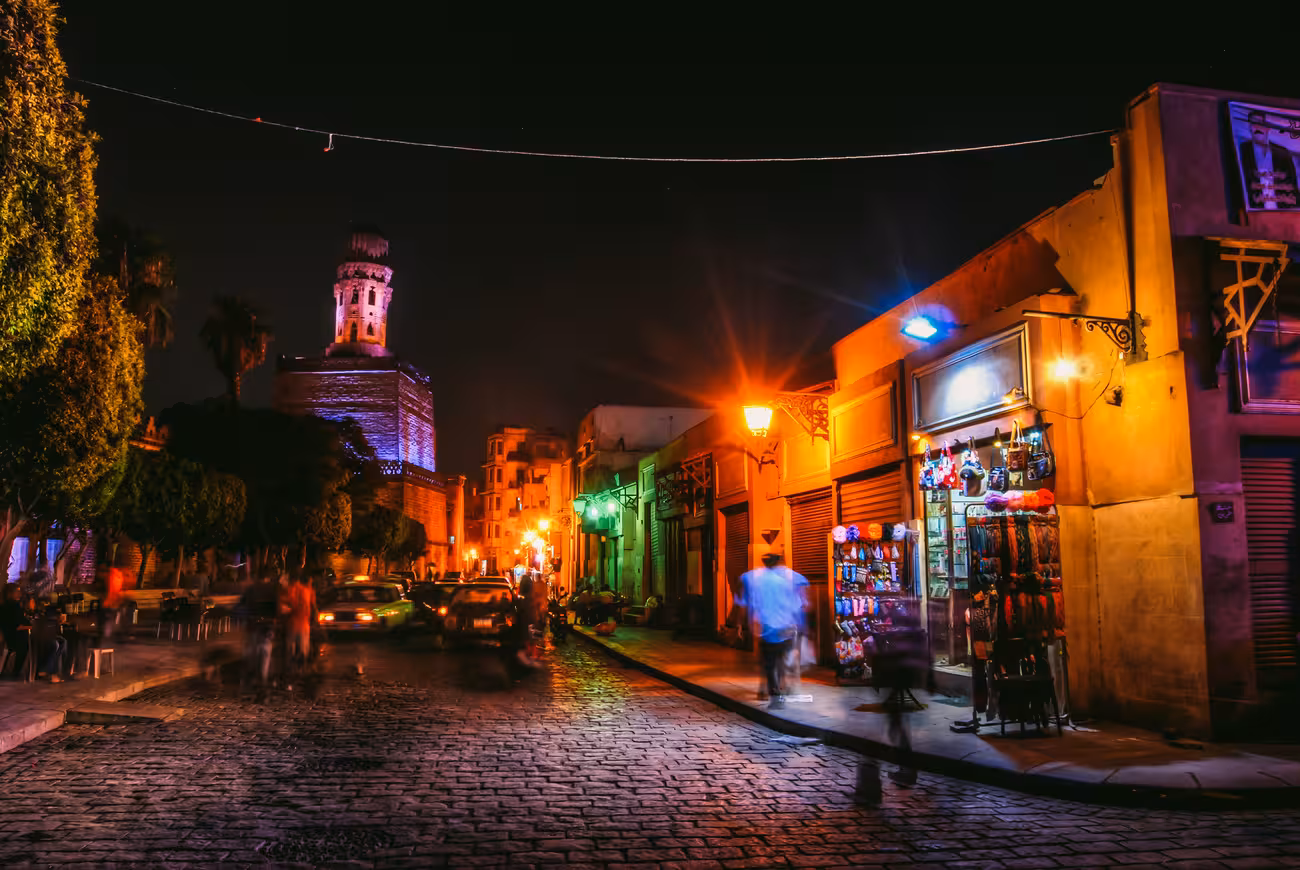 Cairo night bazaar street near historic mosque tower, vibrant lights and shops on Egypt Nile cruise tour