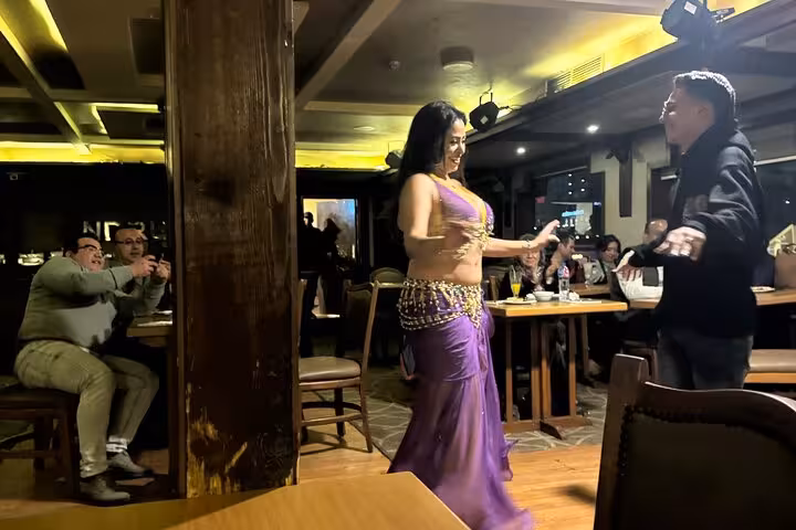 Guest joins belly dancer during Cairo Nile dinner cruise with live show, dining tables and hotel pickup