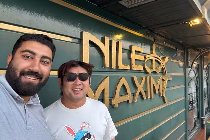 Travelers pose by Nile Maxim boat sign before Cairo Nile dinner cruise with hotel pickup and show