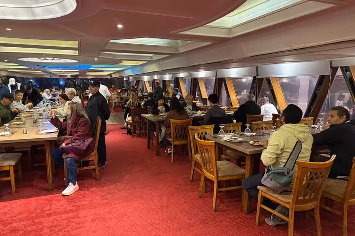 Indoor dining hall on Cairo Nile dinner cruise with seated guests and panoramic windows, includes hotel pickup transfer