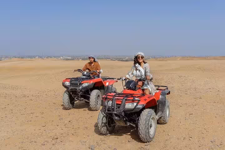 Travelers riding red quad bikes across Cairo desert dunes on a Giza ATV tour before Nile dinner cruise