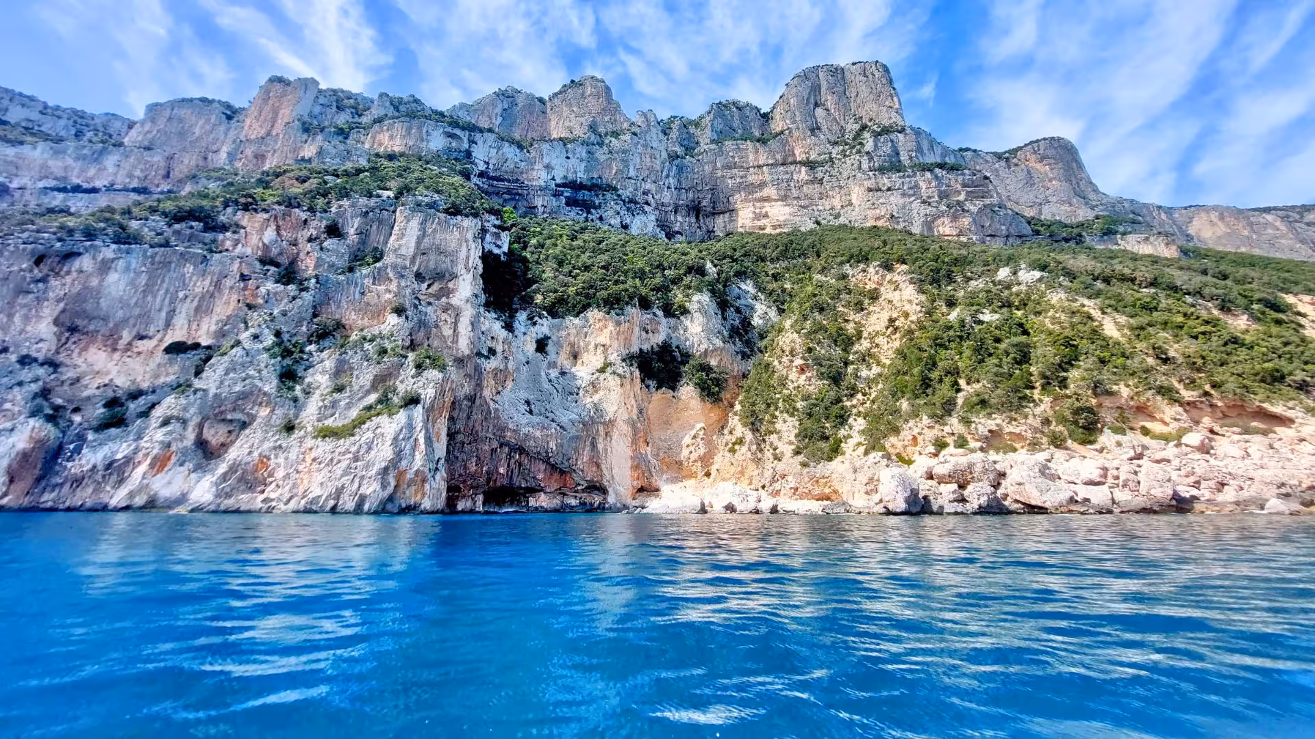 Majestic cliffs covered in lush greenery rise above the clear blue waters of the Gulf of Orosei.