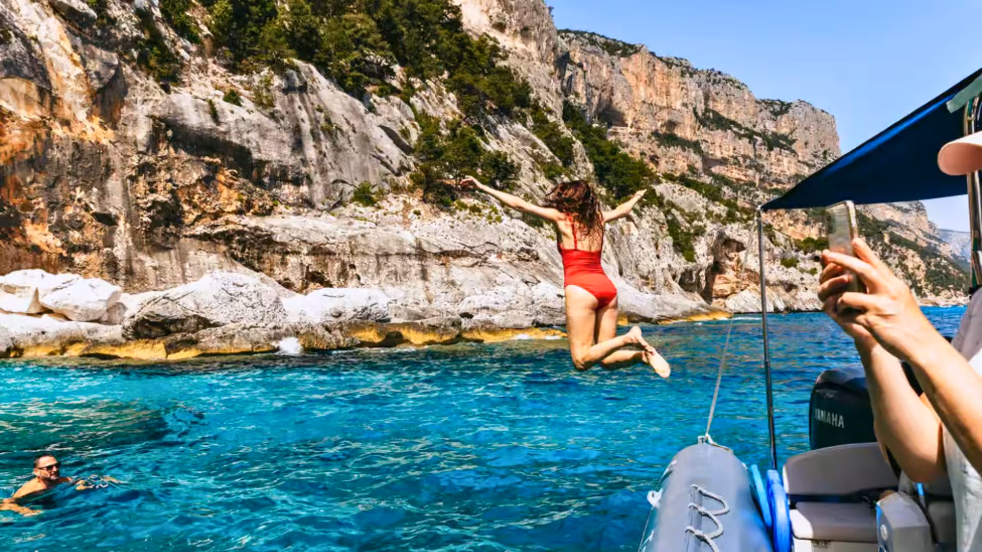 Tourists enjoy a thrilling dive into the turquoise waters of the Gulf of Orosei from a dinghy near Cala Gonone.