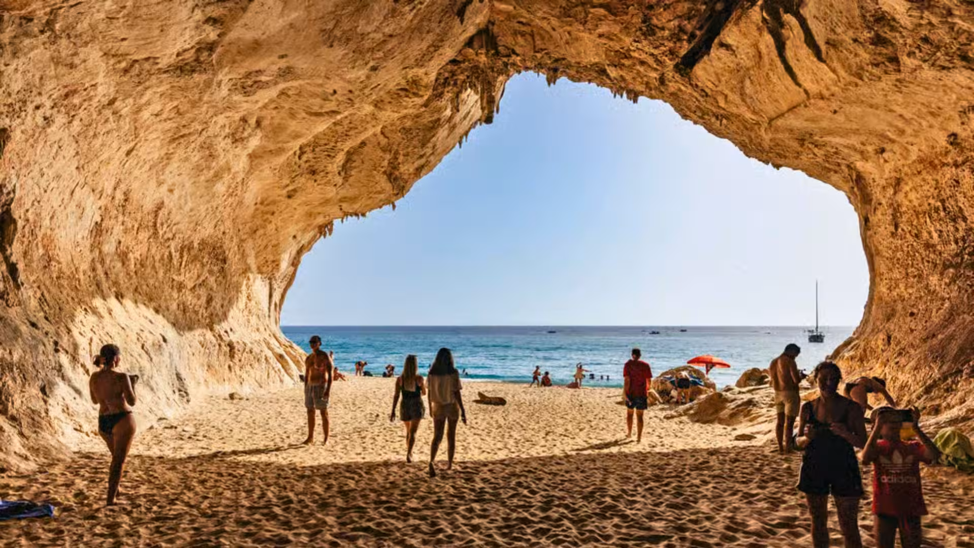 Tourists explore a stunning sea cave opening to a sandy beach in the Gulf of Orosei near Cala Gonone.