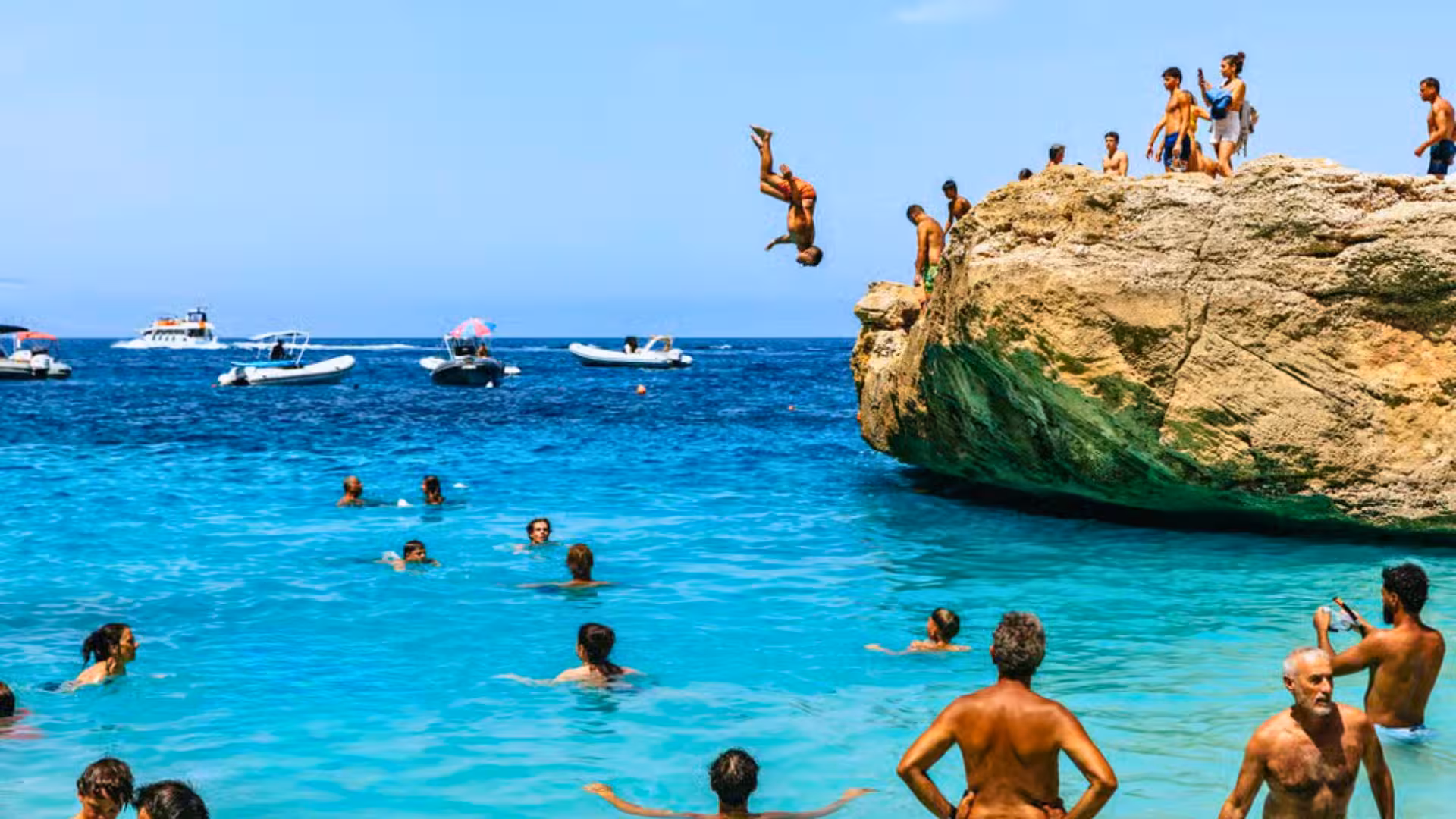 Adventurers cliff diving and swimming in the turquoise waters of the Gulf of Orosei, Sardinia.