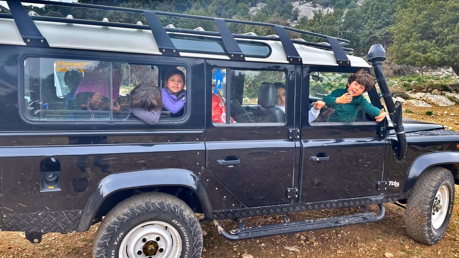Children smiling inside a rugged off-road vehicle during a trekking tour near Cala Gonone.
