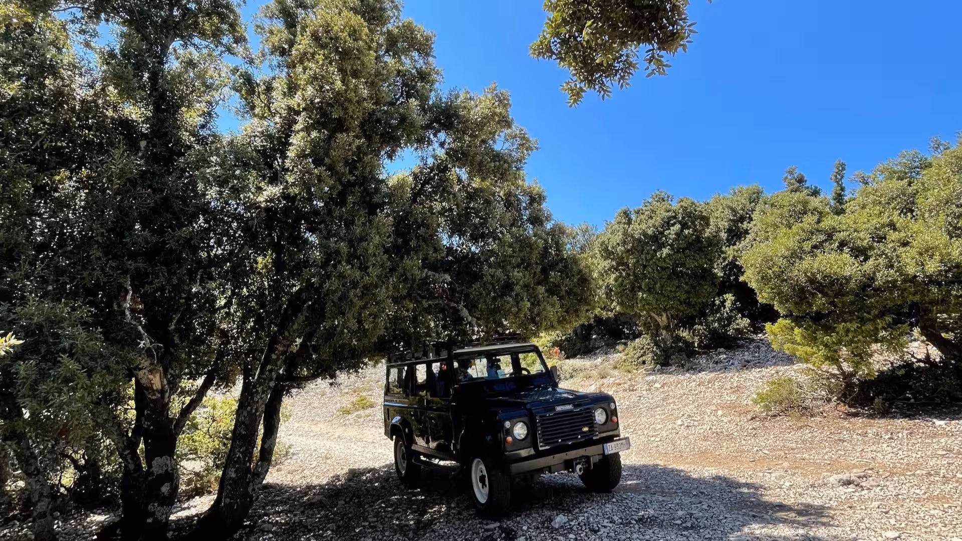 Off-road vehicle parked under shaded trees on a sunny day, ready for adventure in the rugged terrain of Cala Gonone.