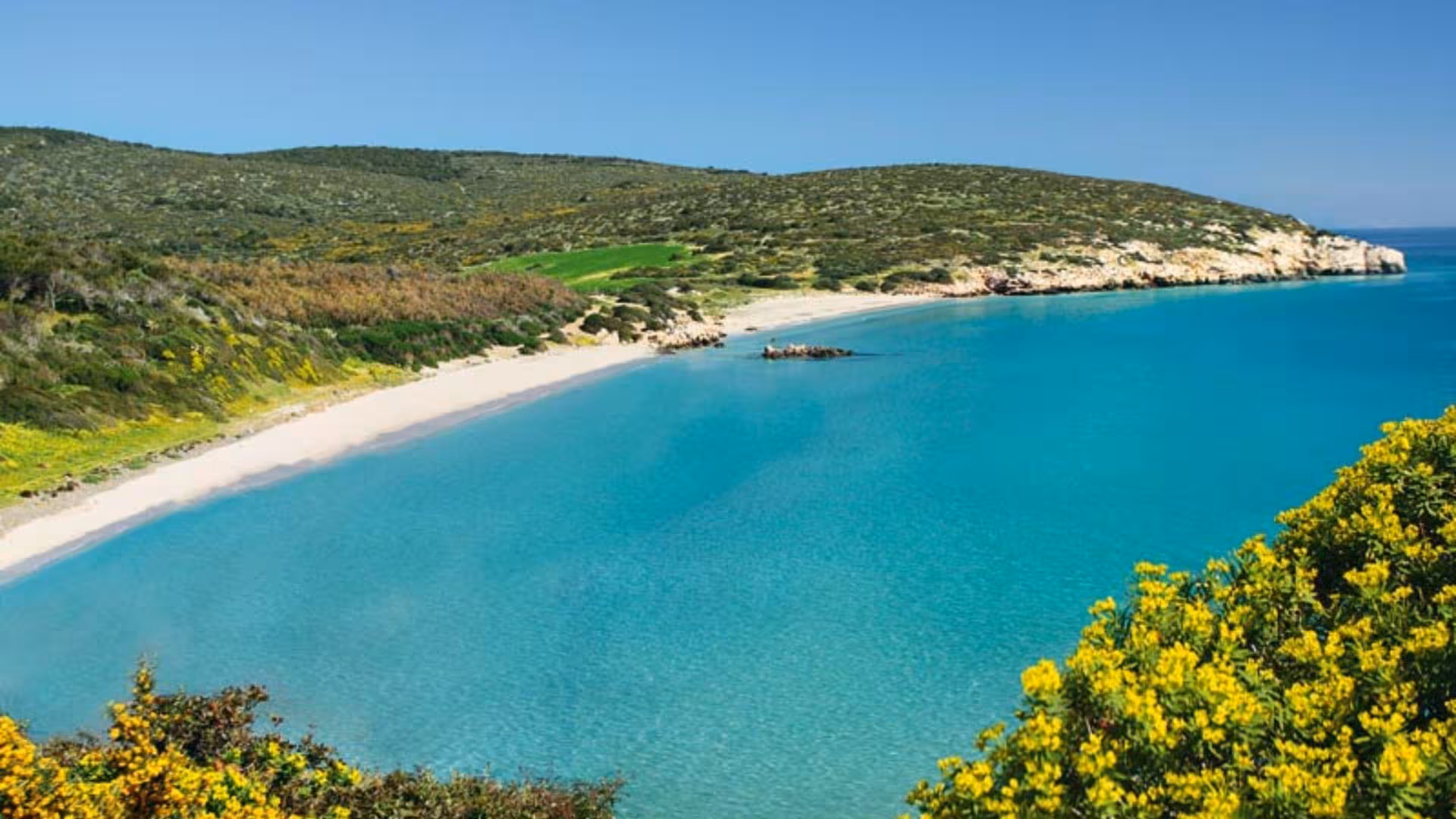 Serene Calasetta beach with clear turquoise waters and lush green hills, ideal for ebike exploration.
