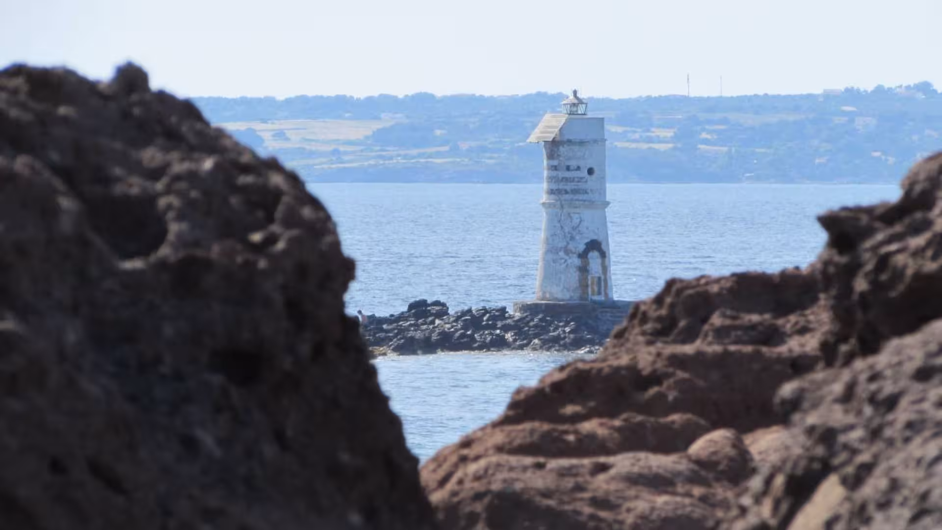 Historic lighthouse view through rocky cliffs in Calasetta, a picturesque stop on an ebike adventure.