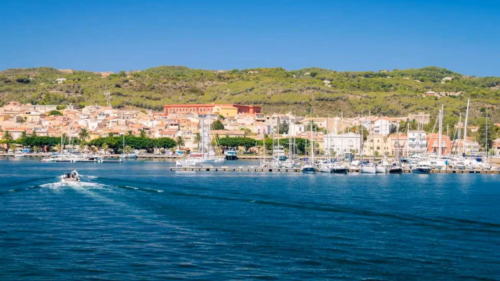 Scenic view of Calasetta harbor with yachts and lush hills, ideal for RIB hire and coastal exploration.