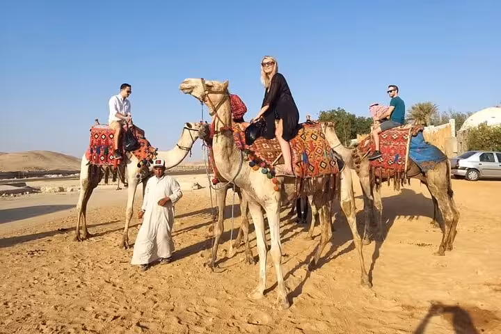 Camel ride in Cairo desert with guides and colorful saddles, part of Giza tour with lunch and shopping