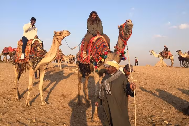 Travelers on decorated camels in Giza desert during Cairo camel ride, lunch, quad bike and shopping tour