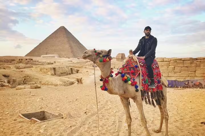 Traveler on decorated camel near Great Pyramid of Giza at sunset, Egypt camel ride tour with transfers