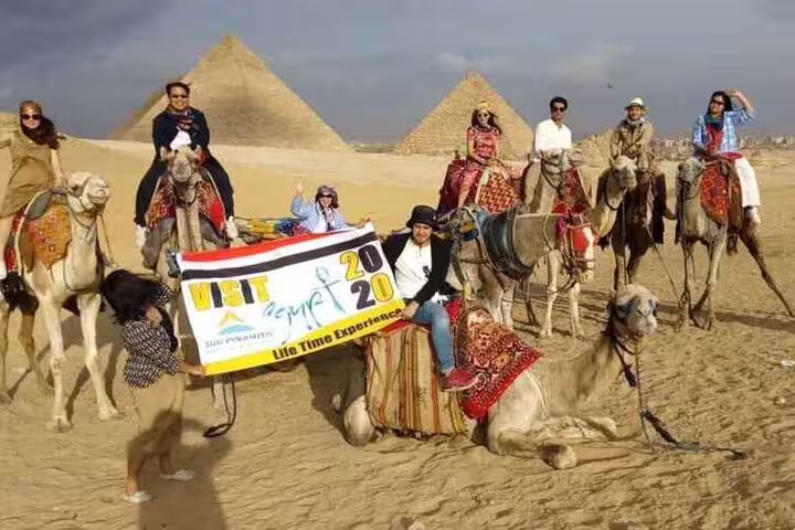 Group camel ride in Giza desert with pyramids backdrop, sunrise or sunset tour experience with transfers