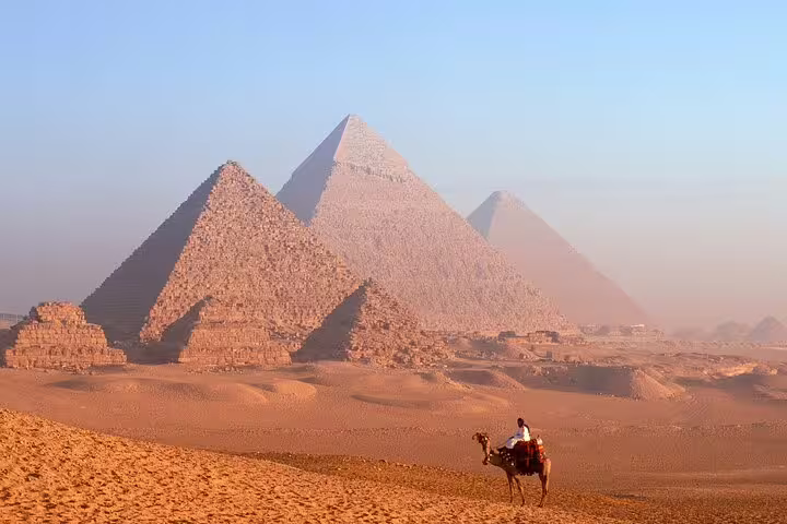 Camel rider in the Giza desert with the Great Pyramids behind, part of a Cairo pyramids tour, museum visit and Nile dinner cruise