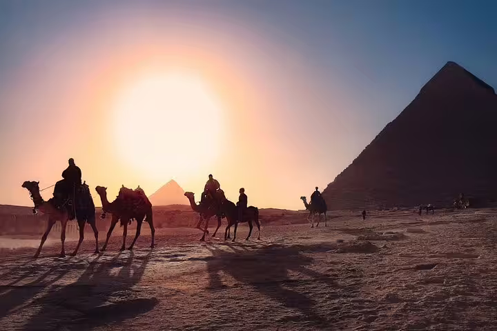 Camel riders at sunset by the Giza Pyramids, included in Pyramids Memphis Saqqara day trip from Cairo