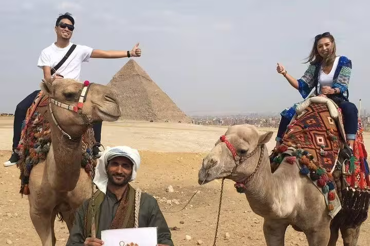 Tourists riding camels at the Pyramids of Giza with local guide, ideal for sunrise or sunset camel tour in Cairo