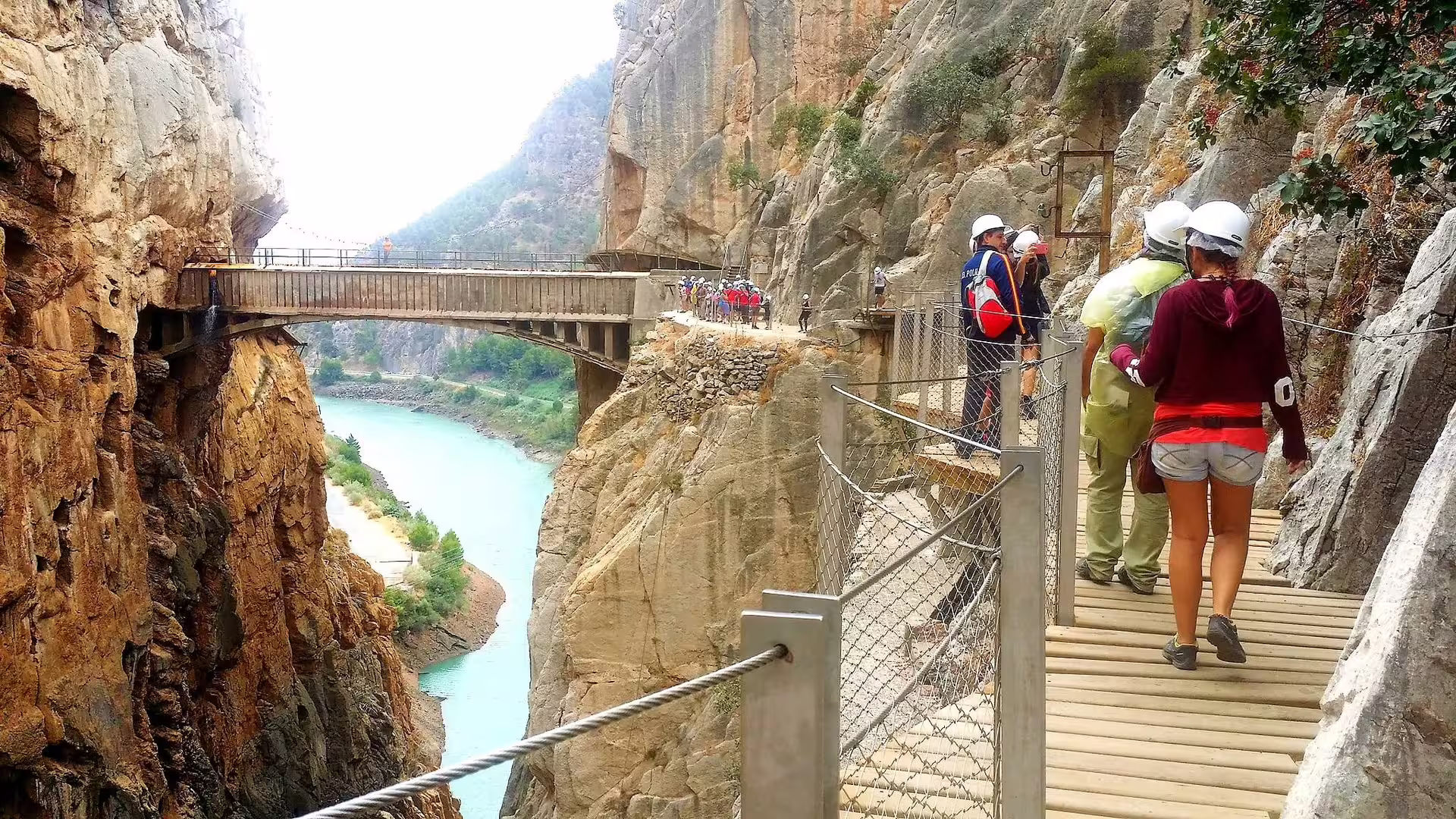 Group walking the Caminito del Rey cliff path above turquoise Guadalhorce River, guided tour in El Chorro gorge
