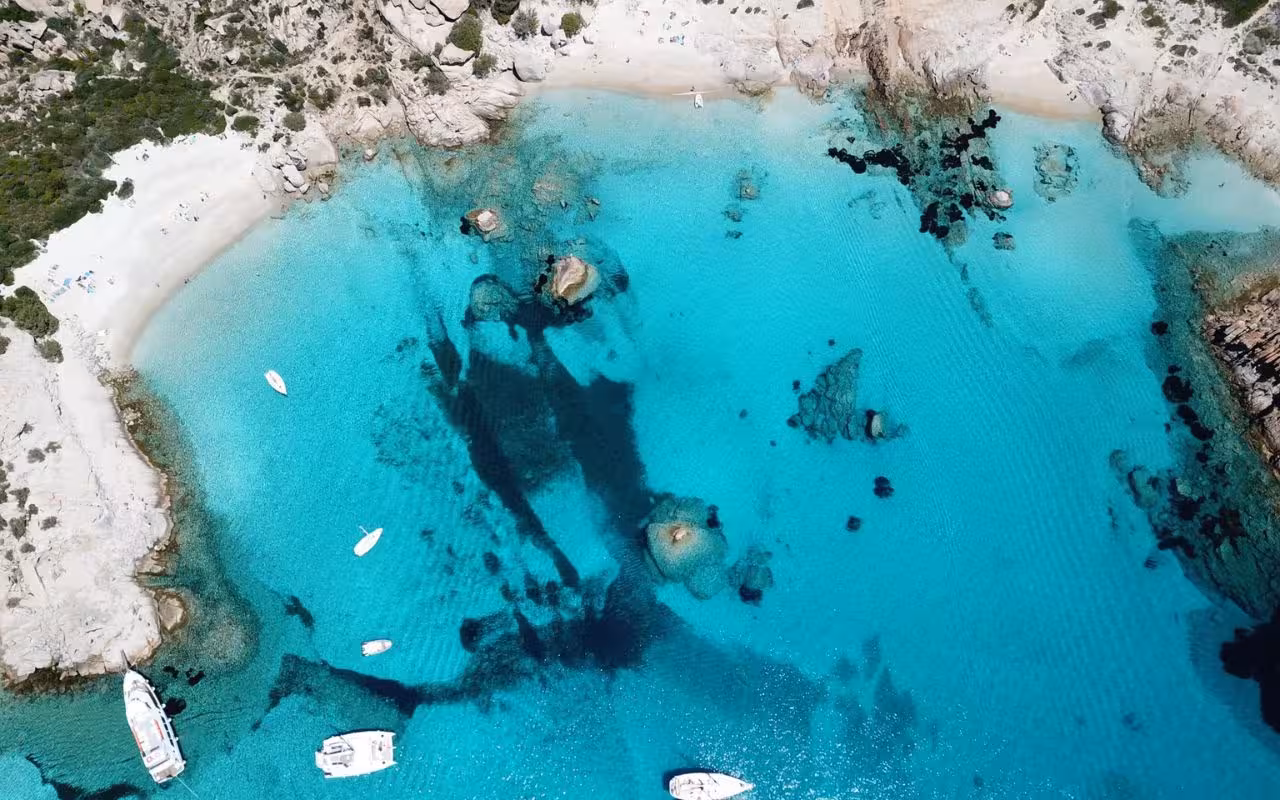 Aerial view of turquoise waters and boats along the sandy shores of La Maddalena Archipelago, perfect for exploring.