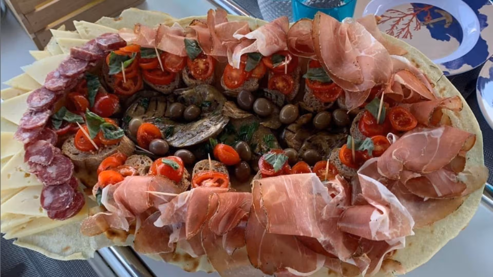 Gourmet platter with cured meats, cheeses, olives, and tomatoes on sailboat tour in La Maddalena Archipelago.