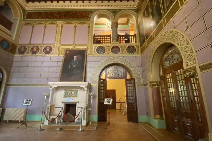 Ornate grand hall interior of Cantacuzino Castle with arched doorways, portrait painting, and decorative fireplace