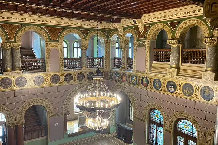 Ornate interior of Cantacuzino Castle with gilded arches, medallions, and chandelier viewed from upper balcony