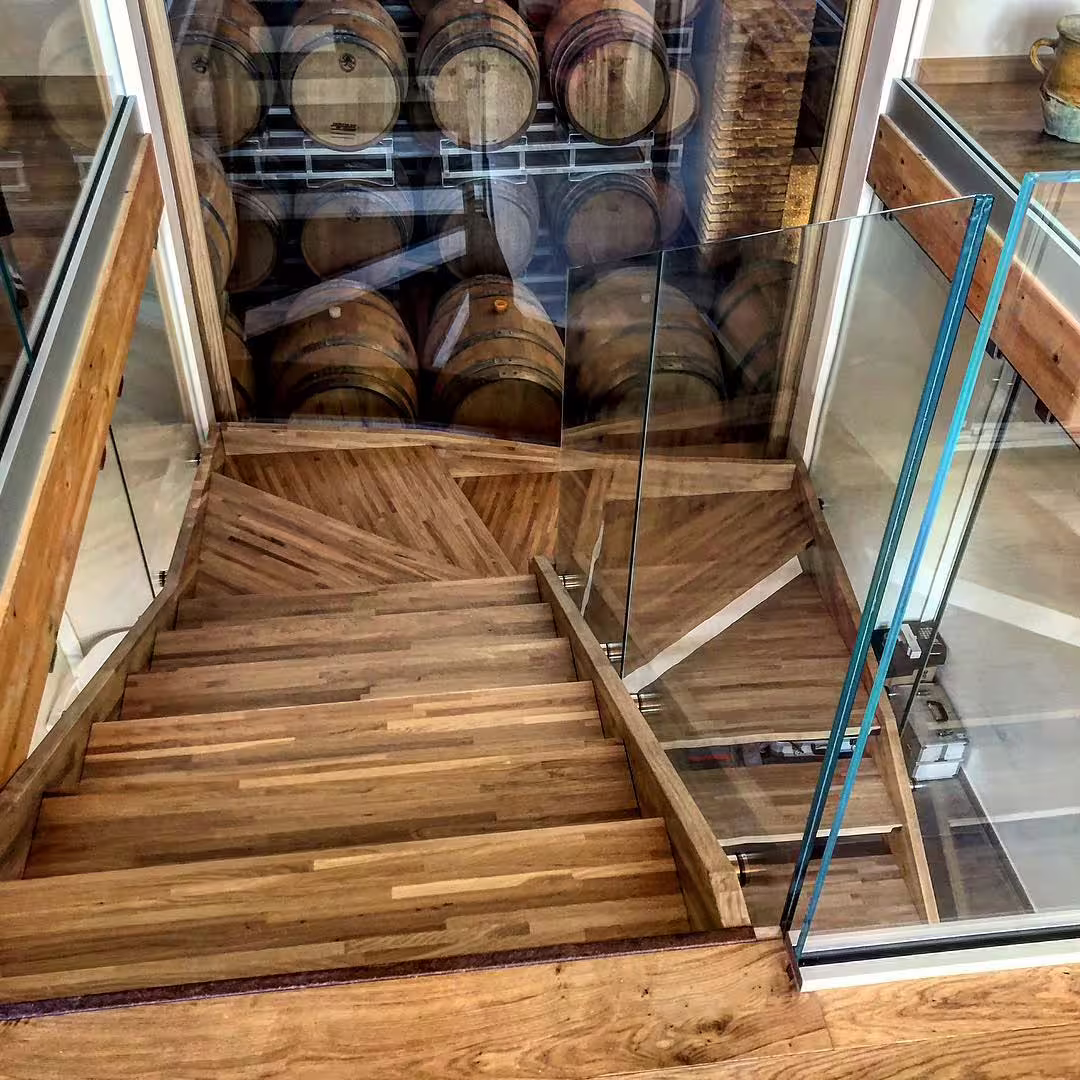 Glass-railed staircase leading to Cantine Mucci wine cellar with oak barrels, part of winery tour and tasting