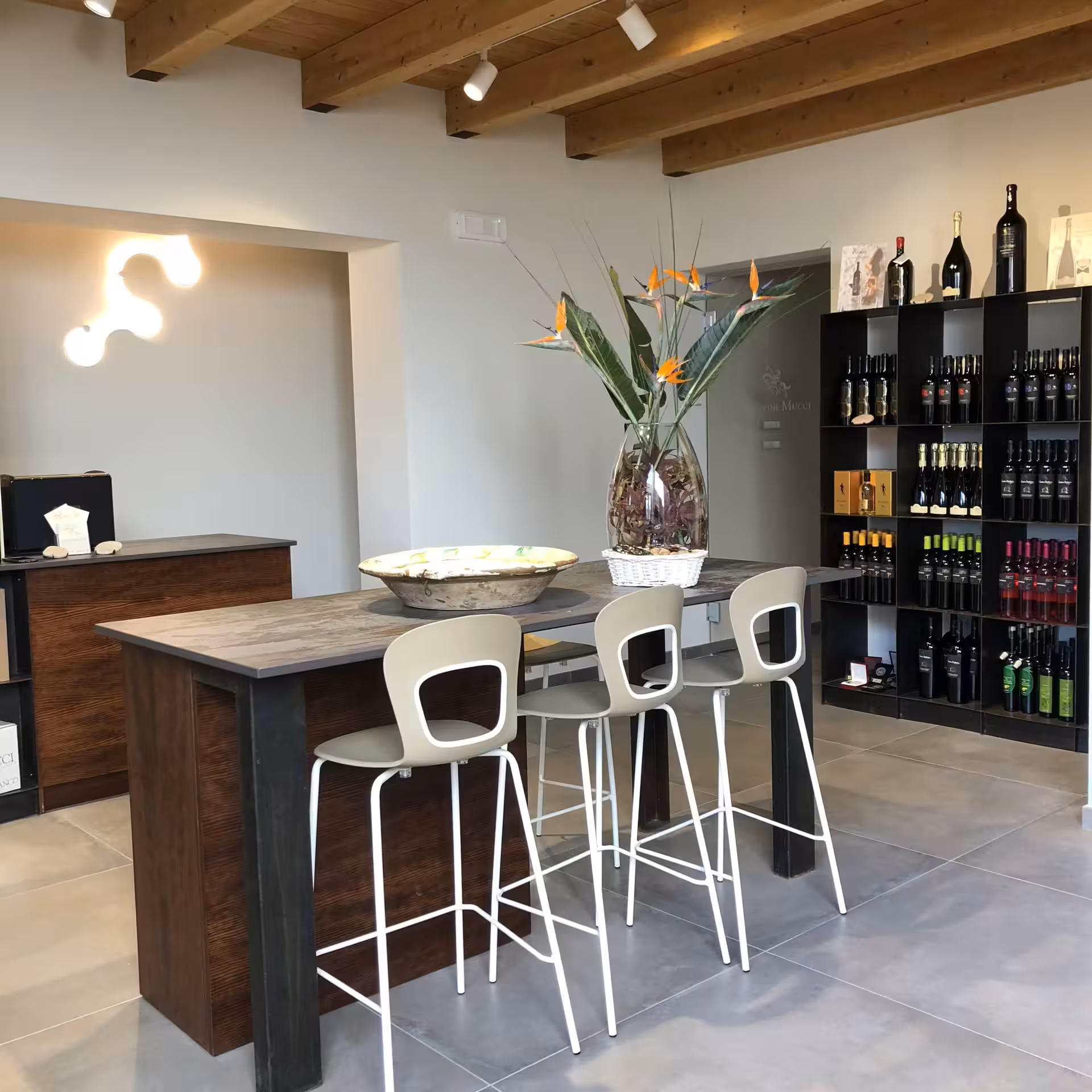 Cantine Mucci wine tasting area with high table, stools and bottle shelves, perfect stop on vineyard stroll tour