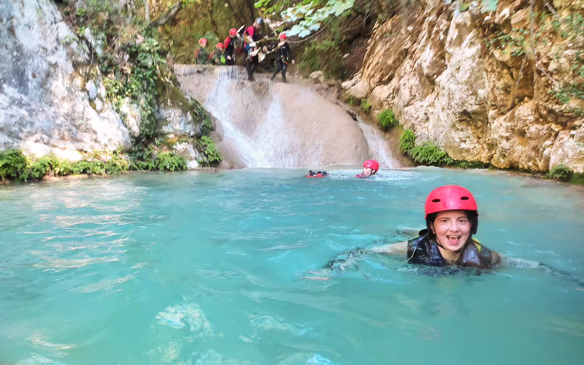 Canyoning at Polylimnio Waterfalls with helmets, swimming in turquoise lagoon beneath a small waterfall