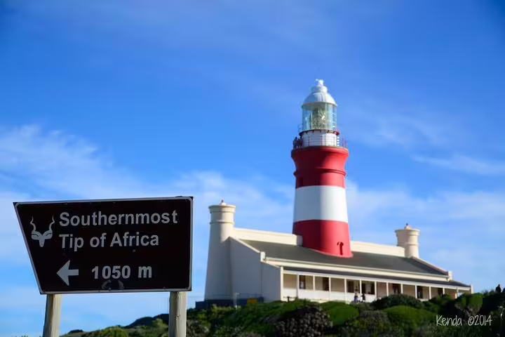Scenic view of Cape Agulhas Lighthouse with sign marking the southernmost tip of Africa under a clear blue sky.