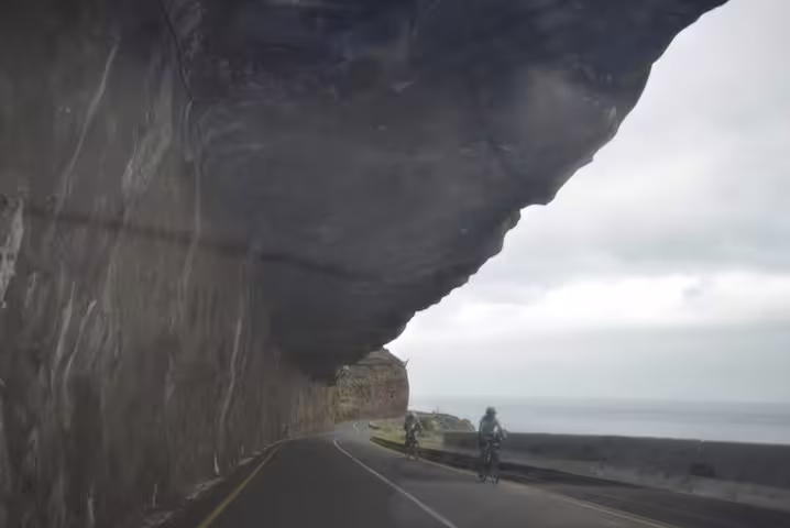 Cyclists riding through a scenic coastal tunnel at Cape of Good Hope, with ocean views and dramatic cliffs.