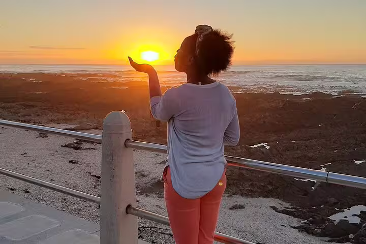 Woman enjoying a breathtaking sunset at Cape of Good Hope, capturing the sun in her hand.
