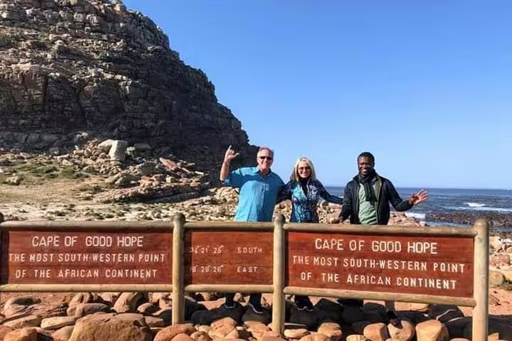 Tourists pose at Cape of Good Hope sign, marking the southwestern tip of Africa's rugged coastline.