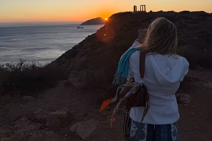 Tourist capturing a stunning sunset at Cape Sounio with Temple of Poseidon silhouette in the background.