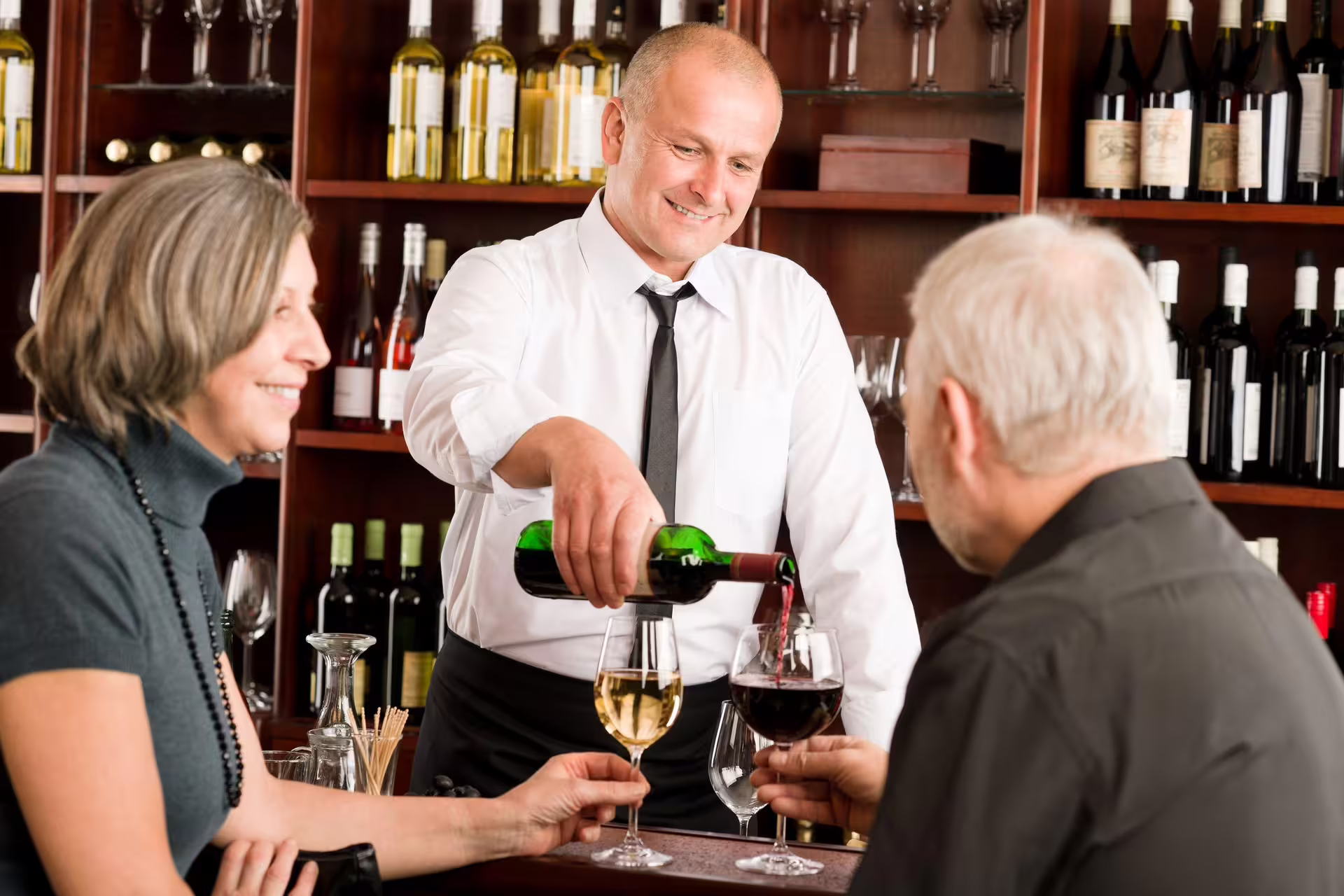 Smiling sommelier pours wine for guests during a Cape Winelands tasting experience.