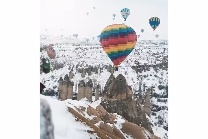 Colorful hot air balloon flying above snowy Cappadocia fairy chimneys on daily tour from Istanbul hotels