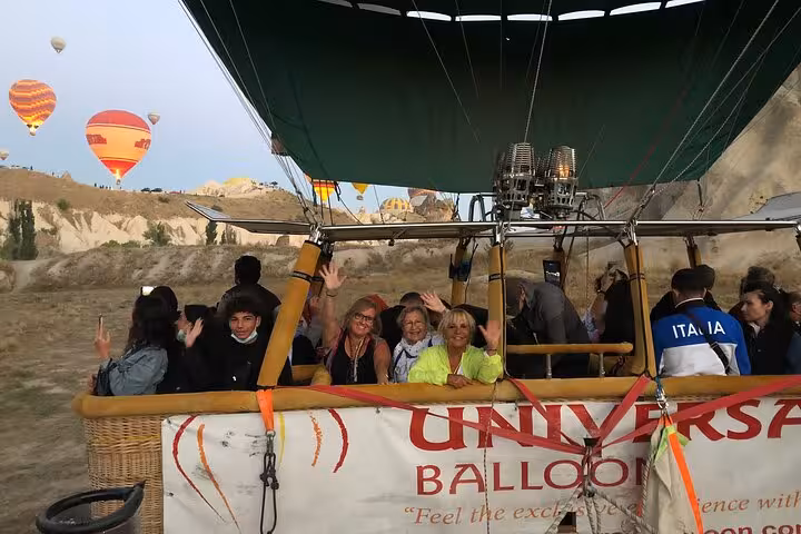 Guests waving from Cappadocia hot air balloon basket with fairy chimneys on private guided luxury tour