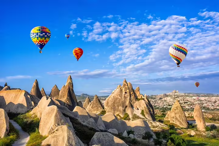 Colorful balloons floating above Cappadocia's rocky terrain, showcasing the beauty of a private tour experience from HOTEL & ASR-NAV airport.