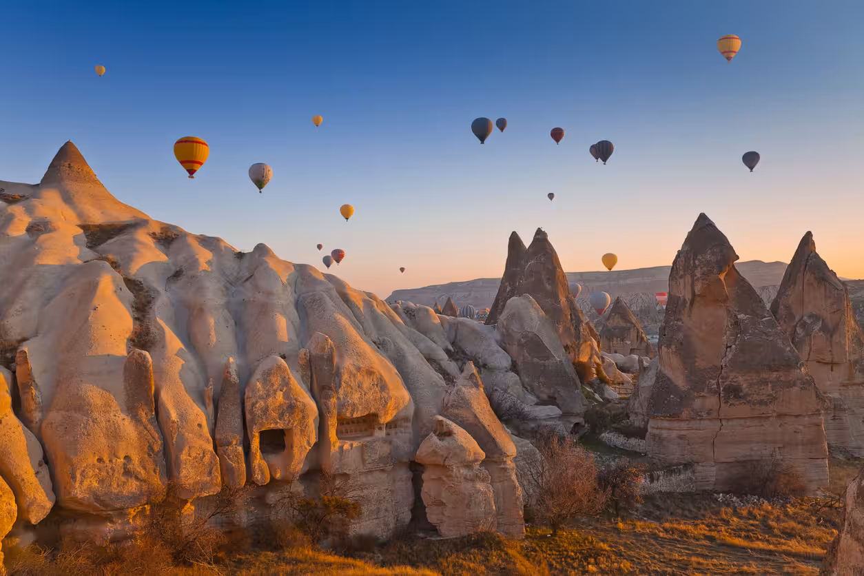Hot air balloons flying over Cappadocia’s orange cliffs and fairy chimneys at sunrise