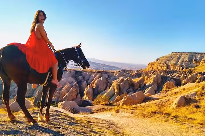 Woman in red dress on horse overlooking Cappadocia valleys at golden hour on a 2-hour sunset ride