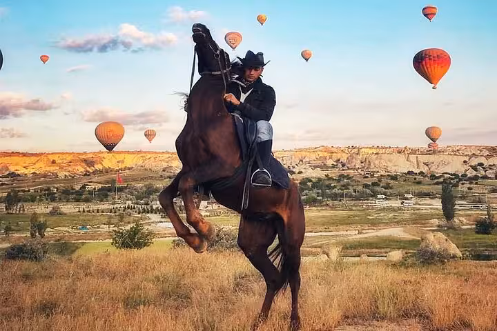Rider on rearing horse with Cappadocia hot air balloons, iconic view on a 2-hour sunset horseback tour