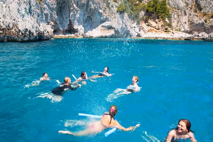Group of people swimming and relaxing in the vibrant turquoise waters of Capri, surrounded by stunning rocky cliffs.