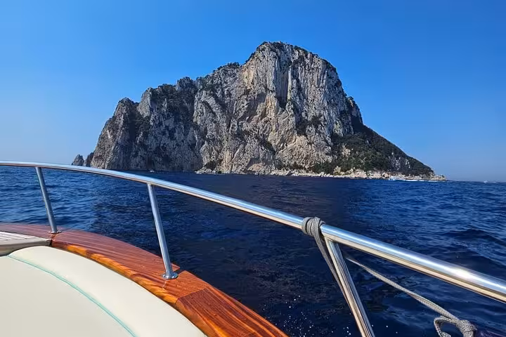 Close-up view from a boat approaching the majestic cliffs of Capri under a clear blue sky.