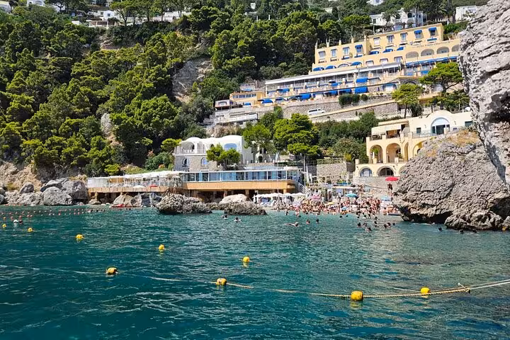 Coastal view of Capri's vibrant architecture and lush greenery from the turquoise waters, ideal for an 8-hour boat tour.