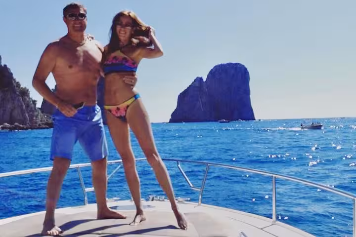 Couple enjoying sunny Capri boat tour with iconic Faraglioni rocks in the background, perfect for summer excursions.